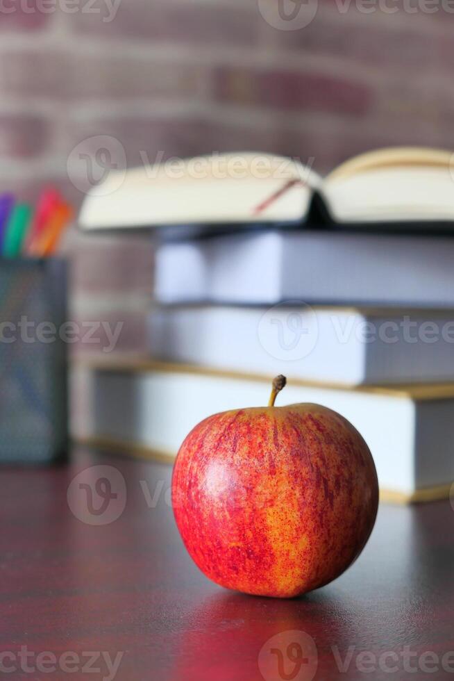 A vibrant red apple placed on a desk, with stacked books beautifully arranged in the background photo