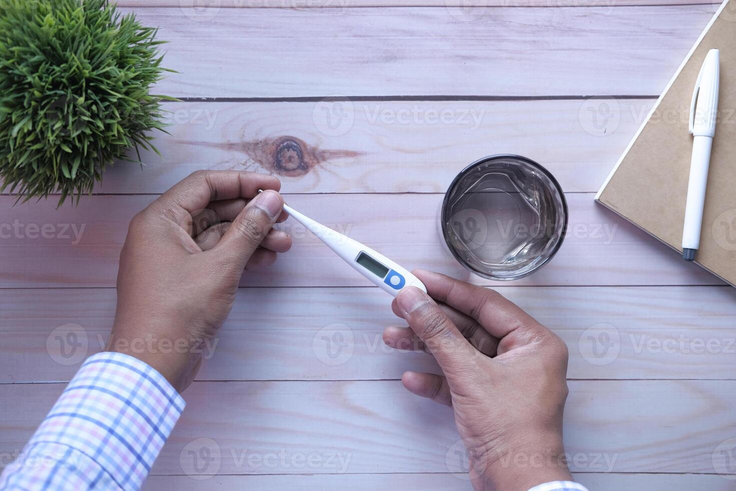 Individual Checking Their Body Temperature Using a Digital Thermometer and a Glass of Water photo