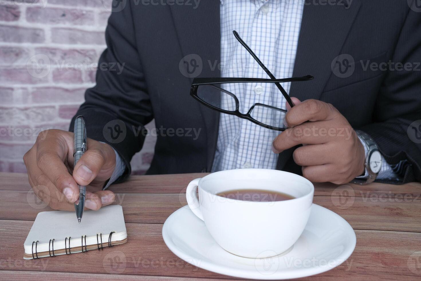 A Professional Man Engaged in Writing Notes While Enjoying Coffee in a Stylish Office Setting photo
