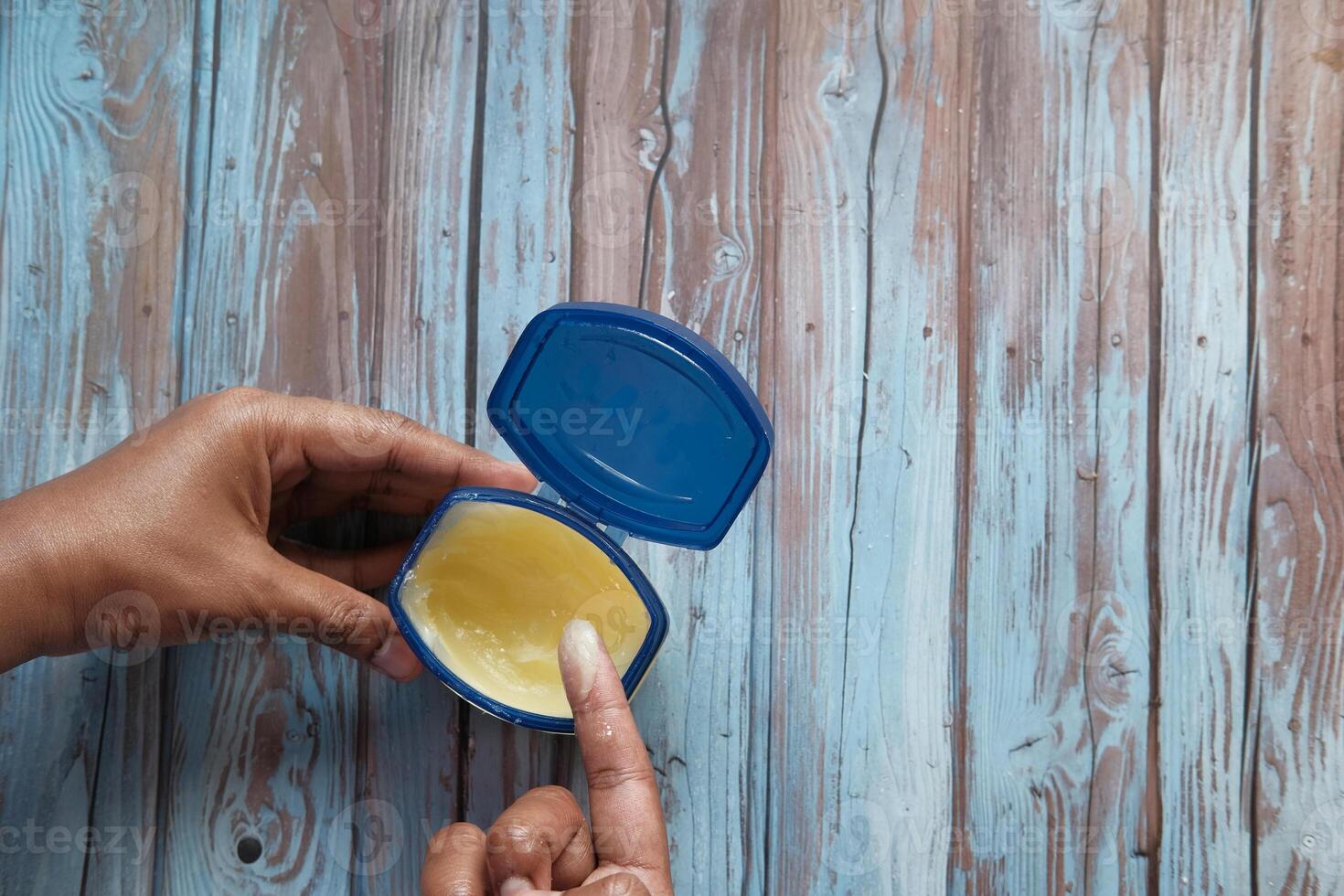 A CloseUp of a Hand Skillfully Applying Cream from an Open Container on a Wooden Table photo