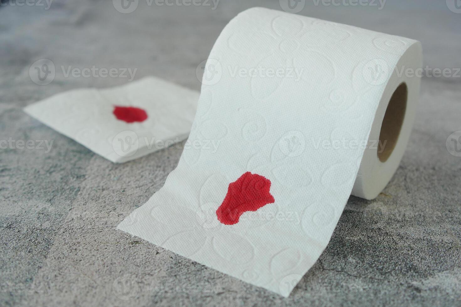 A blood spot is noticeable on a tissue next to a roll of toilet paper in the background photo