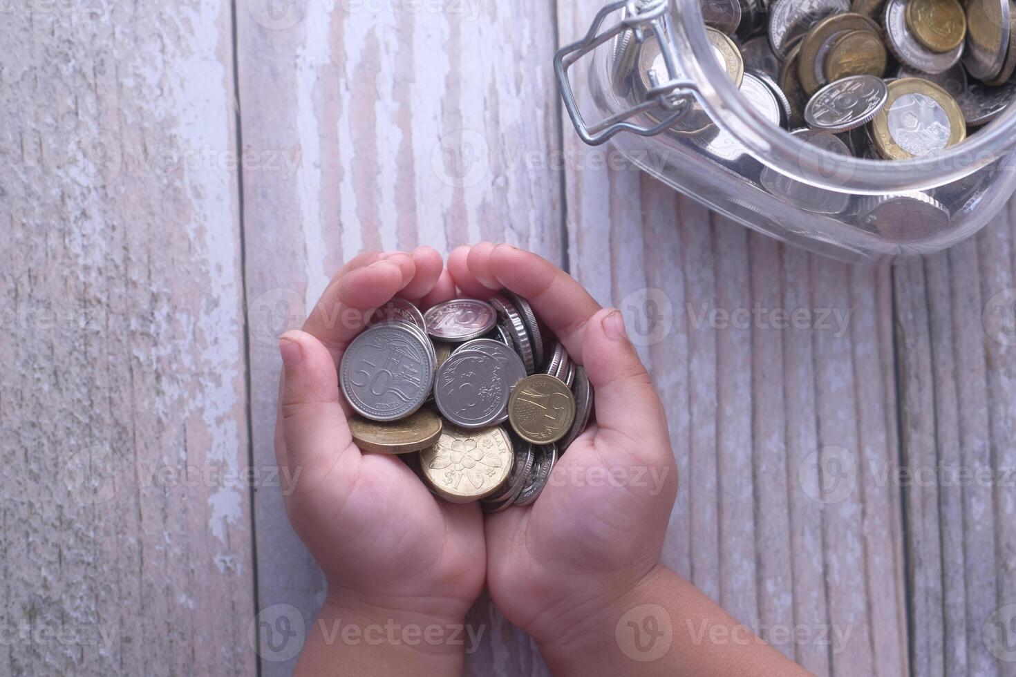 Two Hands Holding a Variety of Coins Next to a Glass Jar Overflowing with Loose Change photo