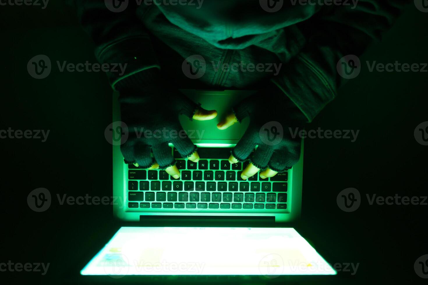 Hands are actively typing on a laptop that features green illumination in a dark environment photo