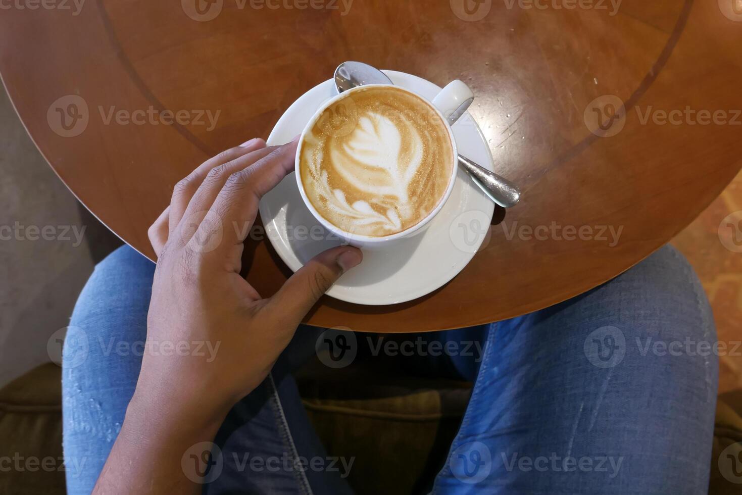 A closeup view of beautifully crafted latte art accompanied by a hand resting on a table photo