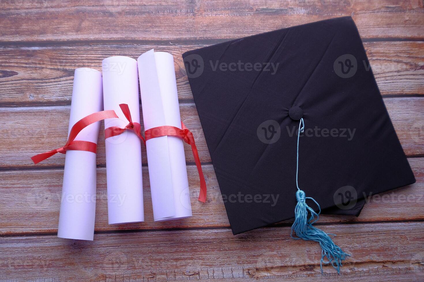 A Graduation Cap and Diplomas are beautifully arranged on an elegant Wooden Table surface photo