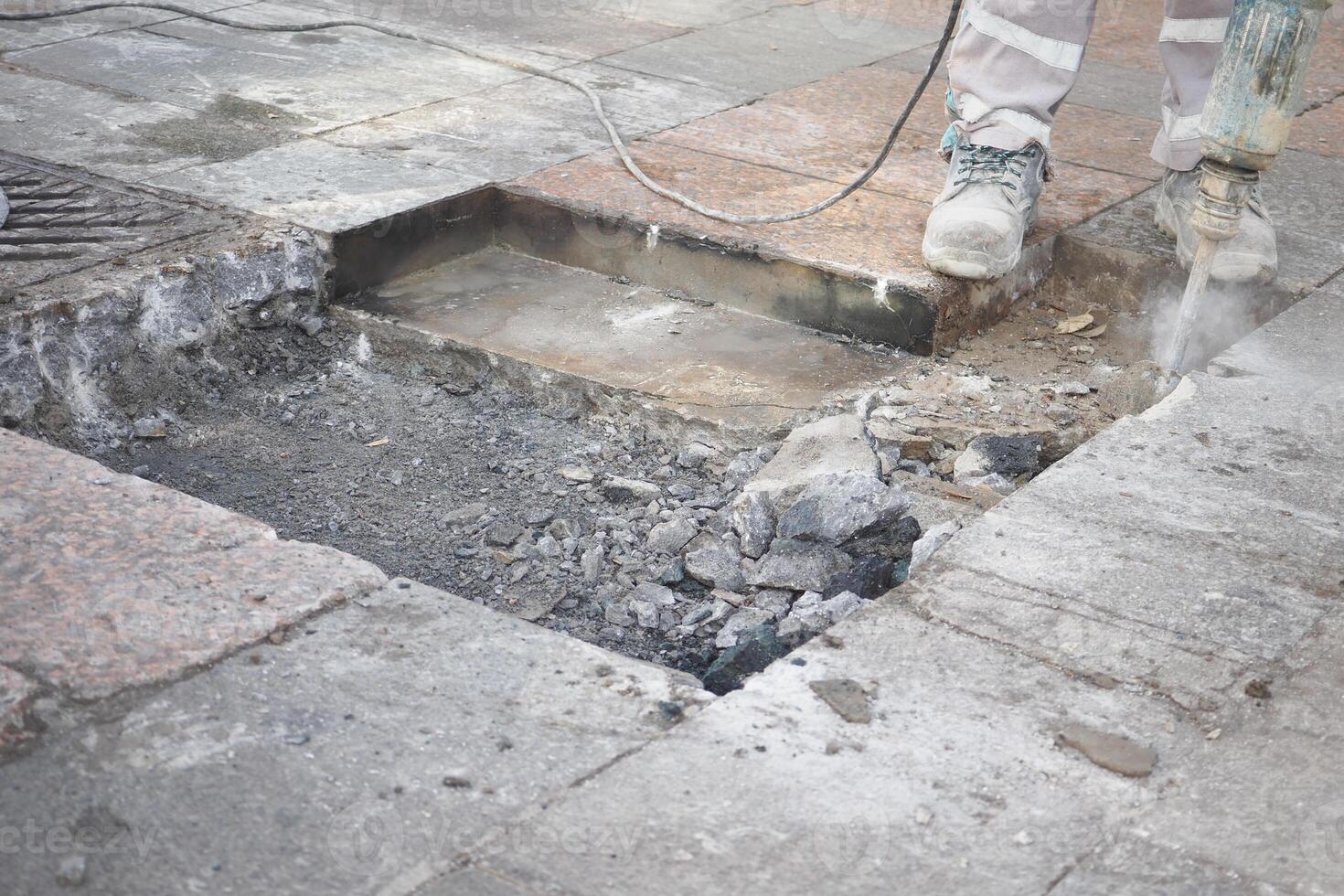 A construction worker is diligently repairing the sidewalk using a powerful jackhammer tool photo