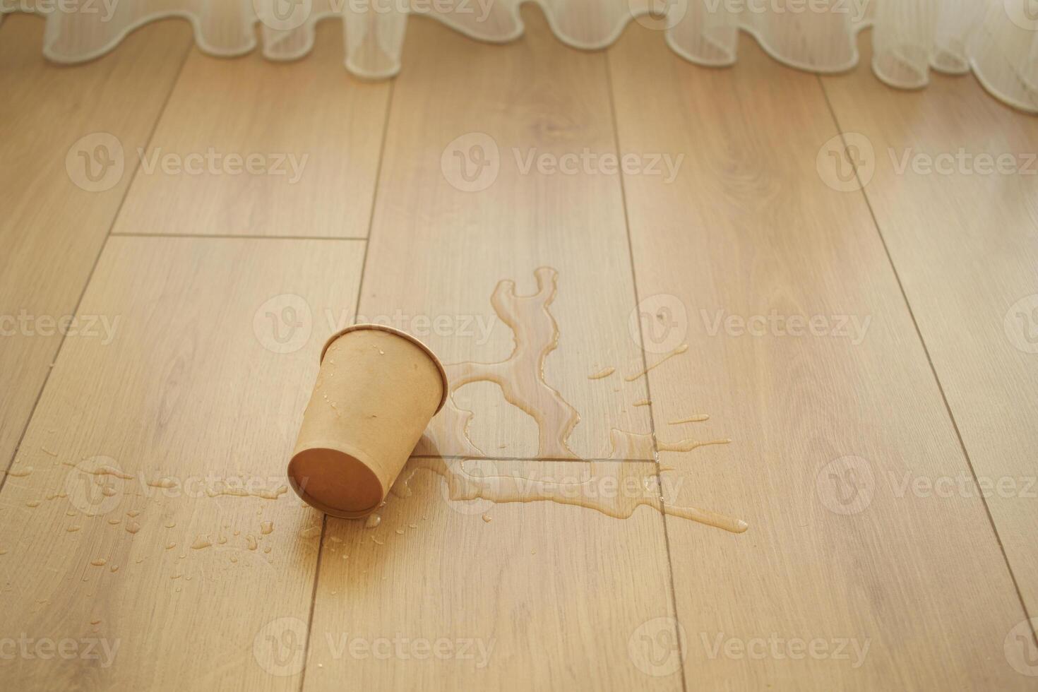 A cup of liquid spilled on a wooden floor resulting in visible water stains appearing photo