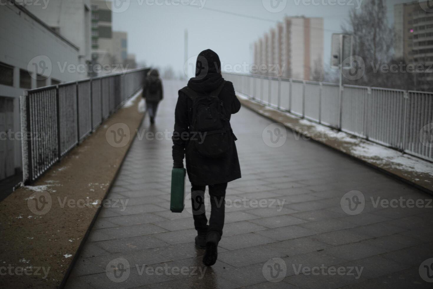 Guy carries suitcase down street.. Man in black clothes on cloudy day. photo
