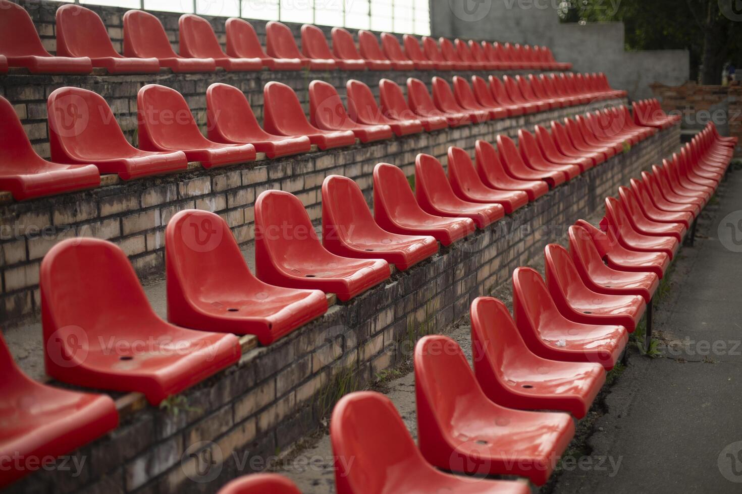 The grandstand at the sports arena. Empty seats in the stadium. Red plastic chairs. photo