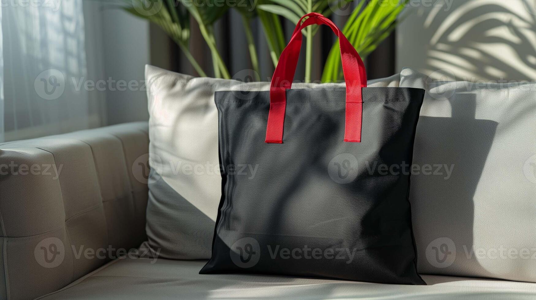 Black tote bag mockup with red handles on gray sofa. Lush green palm leaves behind couch totebag template advertising image. Modern design shopper mock up product photorealistic photo