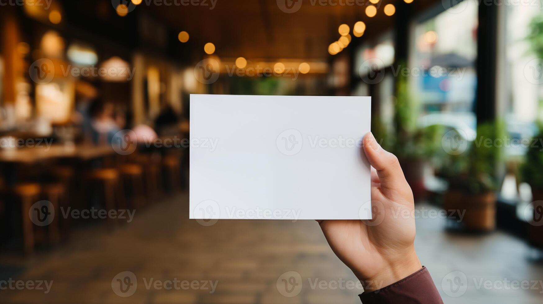 Hand displaying blank card mockup in modern outdoor cafe. Coffeeshop natural lighting. Business promotion template advertising image. Invitation mock up product photorealistic photo