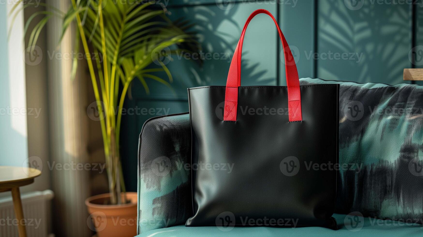 Black leather tote bag mockup with red handles on stylish couch. Teal interior with potted plant. Modern totebag template advertising image. Luxury shopper mock up product photorealistic photo