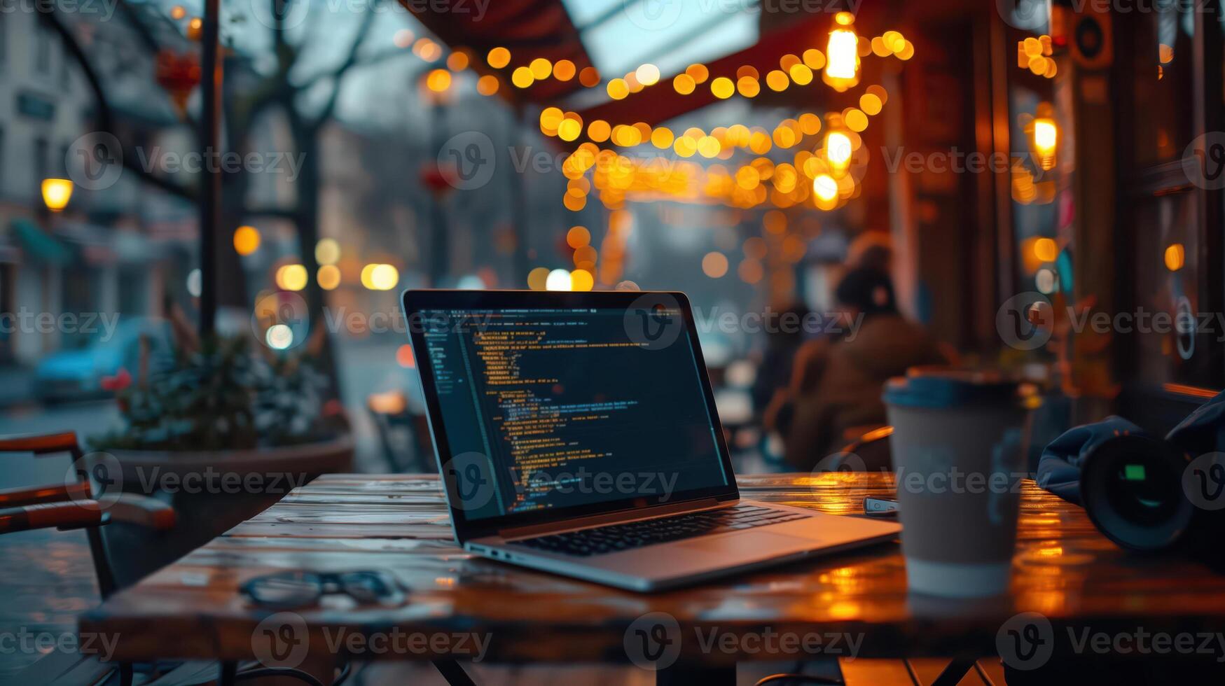 Coding laptop on outdoor cafe table at twilight with warm festive lights in background photo