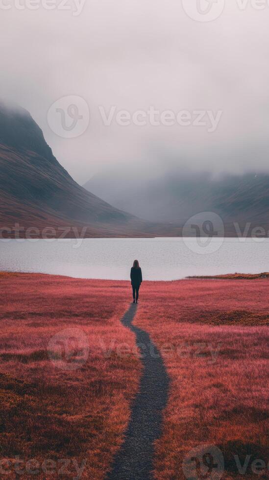 A person walking down a path in a field with a lake in the background photo
