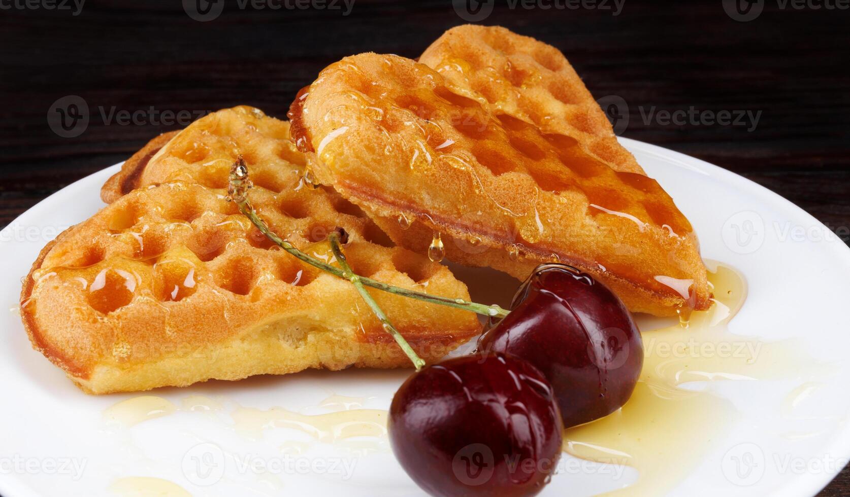 Viennese waffles with cherries lie on a white plate. Viennese waffles drizzled with honey in the shape of a heart. photo