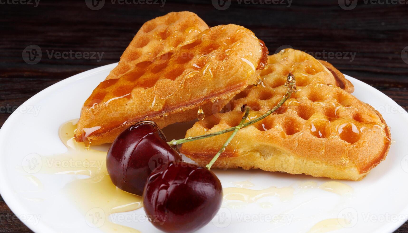 Viennese waffles with cherries lie on a white plate. Viennese waffles drizzled with honey in the shape of a heart. photo