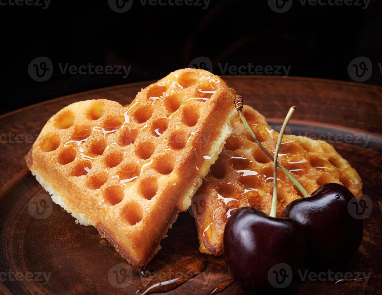 Heart-shaped Viennese waffles drizzled with honey lie on a clay plate. Viennese waffles with cherries. photo