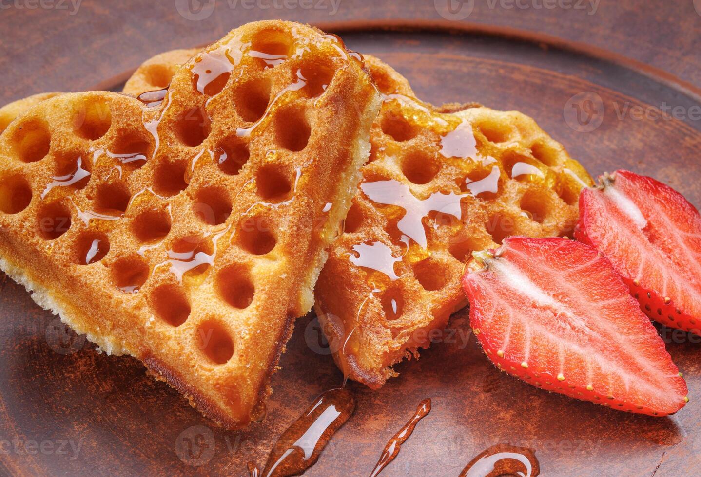 Viennese waffles drizzled with honey in the shape of a heart lie on a clay plate. Viennese waffles with cut strawberries. photo