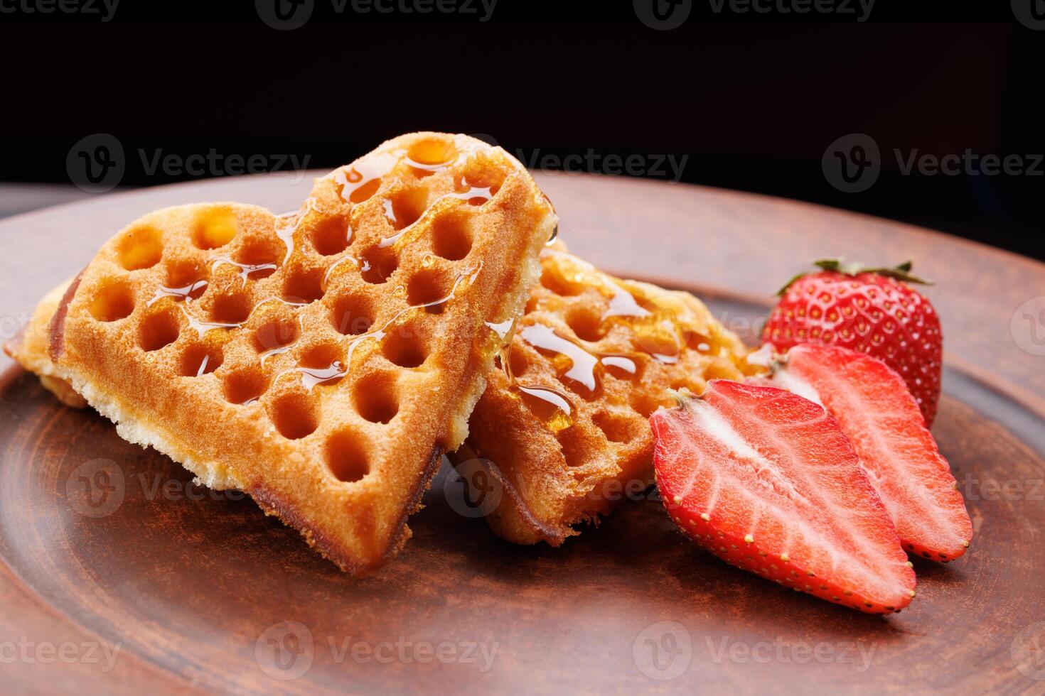 Viennese waffles drizzled with honey in the shape of a heart lie on a clay plate. Viennese waffles with cut strawberries. photo