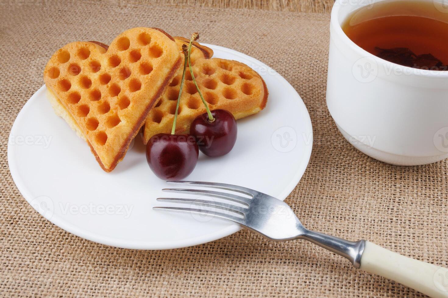 Viennese waffles with cherries lie on a white plate. Viennese waffles in the shape of a heart. photo