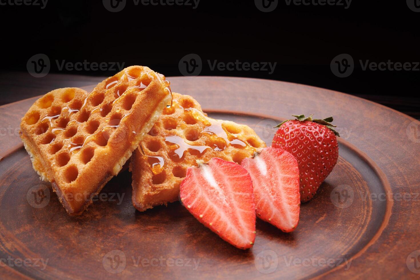 Viennese waffles drizzled with honey in the shape of a heart lie on a clay plate. Viennese waffles with cut strawberries. photo