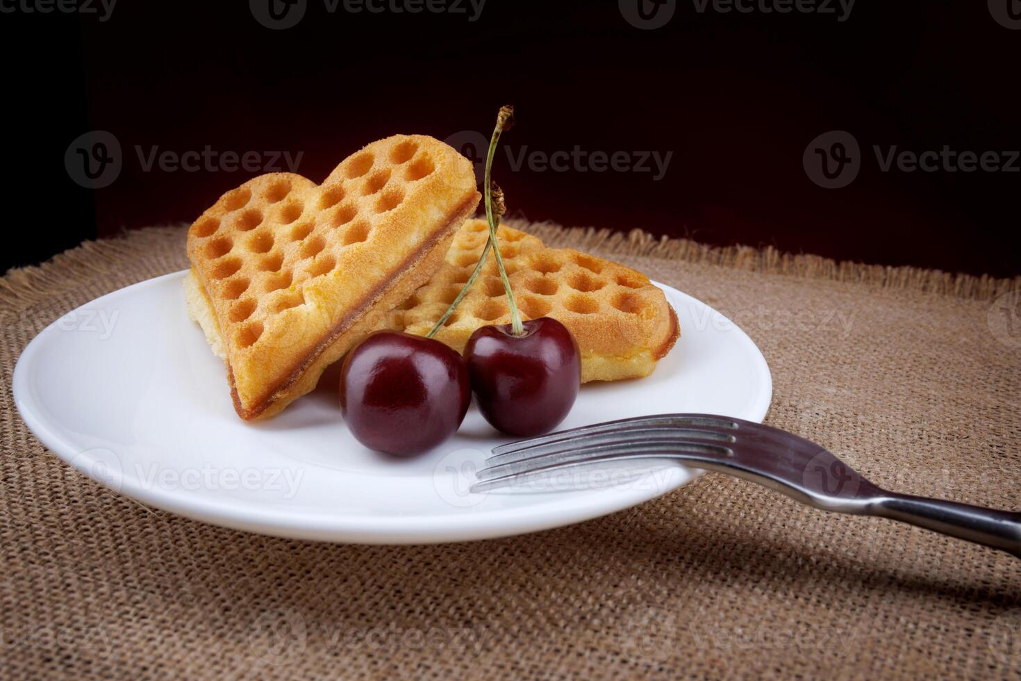 Viennese waffles with cherries lie on a white plate. Viennese waffles in the shape of a heart. photo