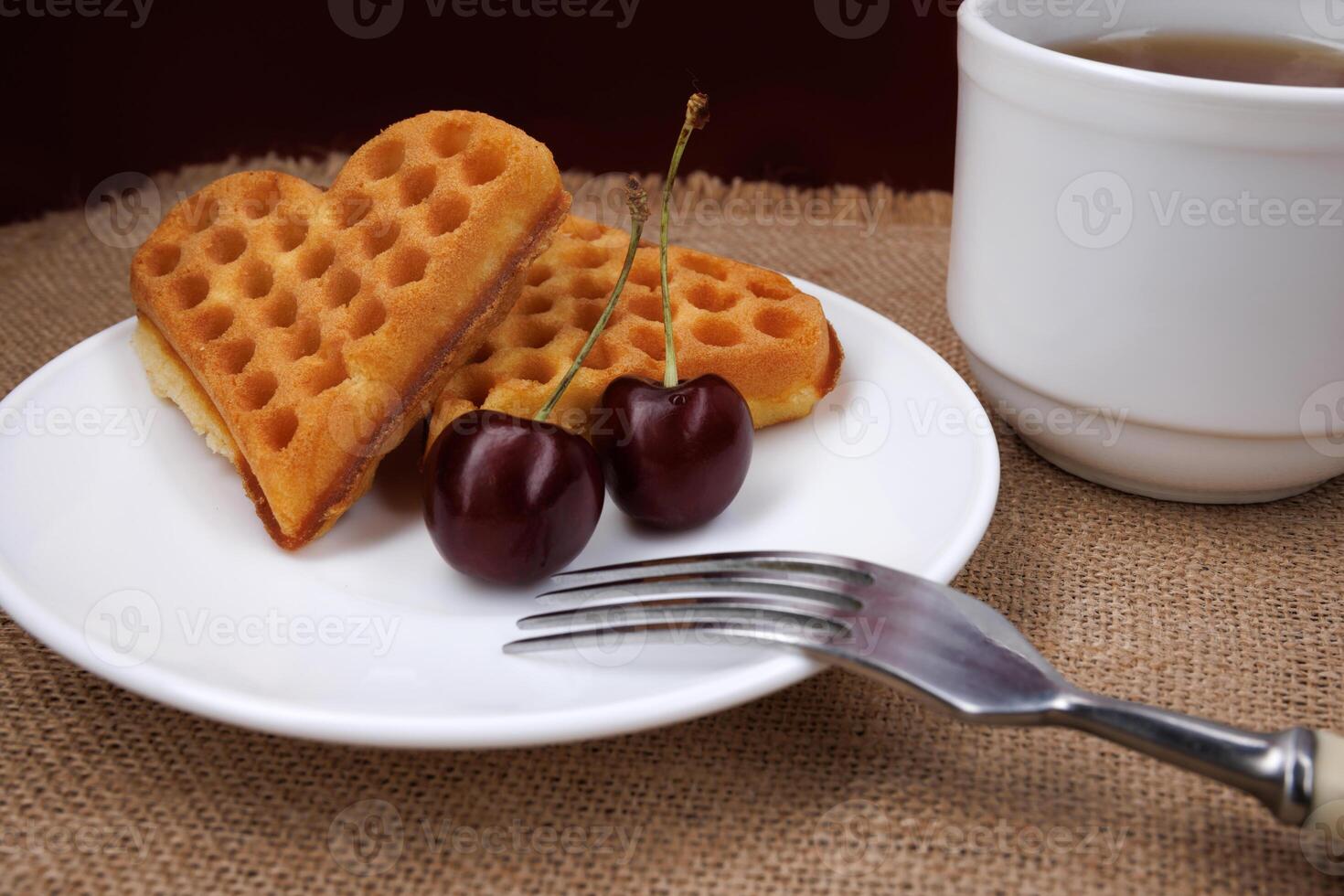 Viennese waffles with cherries lie on a white plate. Viennese waffles in the shape of a heart. photo