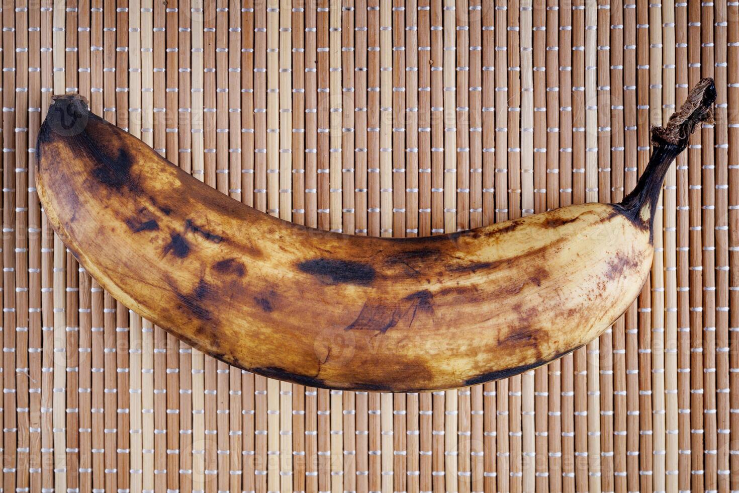 An overripe banana lies on a bamboo napkin. photo