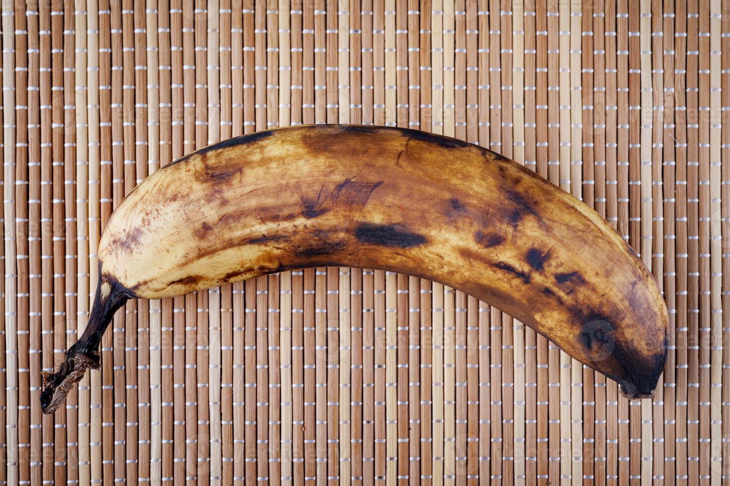 An overripe banana lies on a bamboo napkin. photo