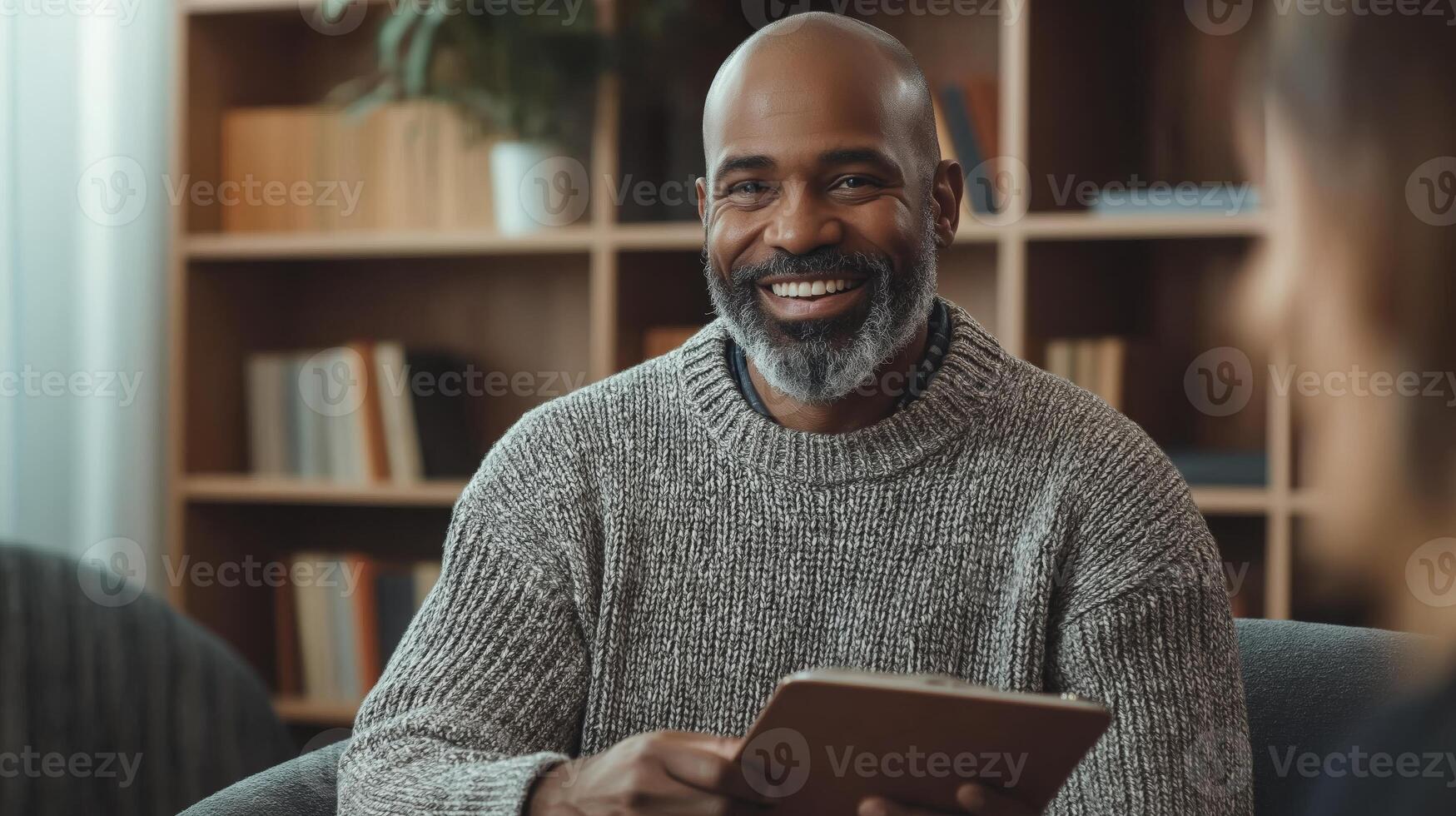 MiddleAged Man of African Descent Smiling, Holding a Tablet in Cozy Library Setting, Perfect for Professional Use in Articles, Blogs, and Social Media Campaigns photo