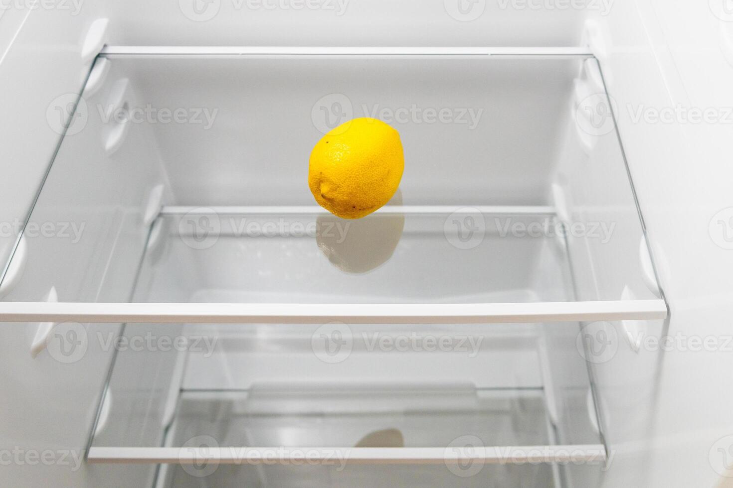 single fresh lemon on glass shelf in refrigerator photo