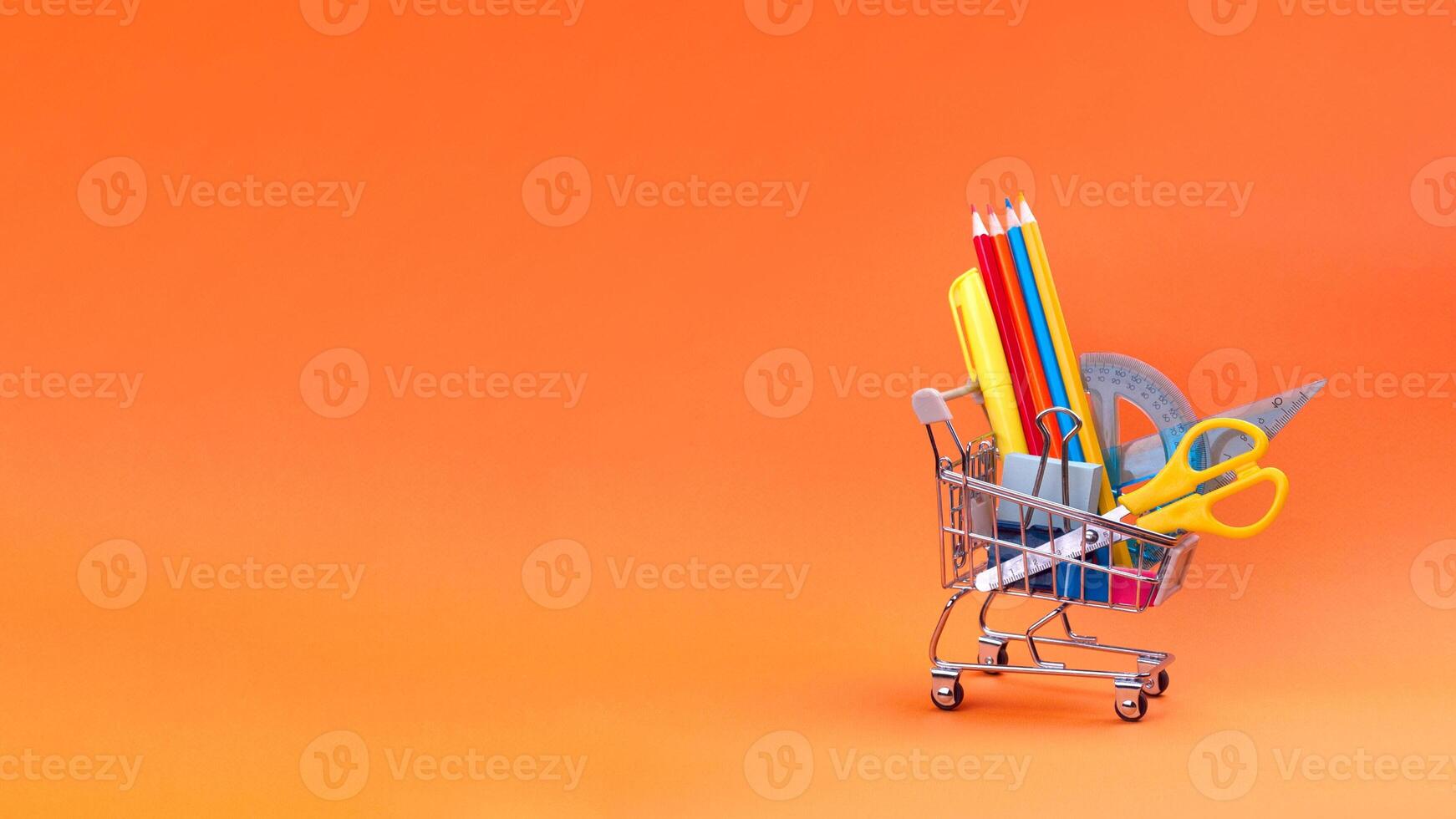 Shopping cart with school supplies on orange background. Preparing for school, buying stationery concept. Banner copy space photo