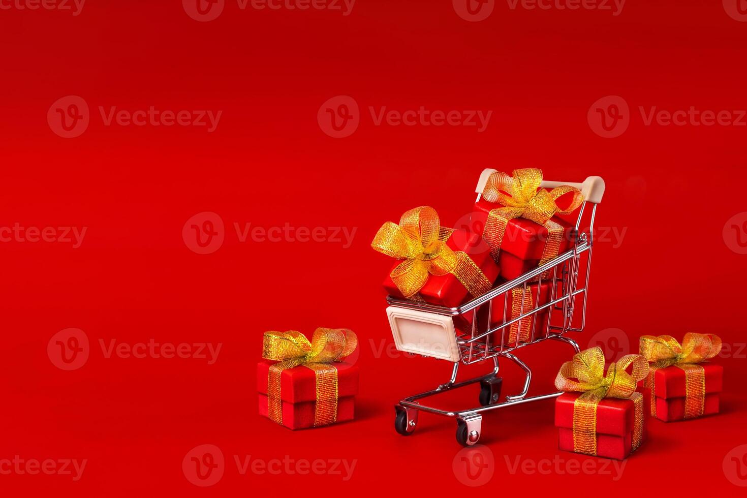 A shopping cart with red gifts with gold bows on a red background. Holidays, gifts, shopping copy space photo