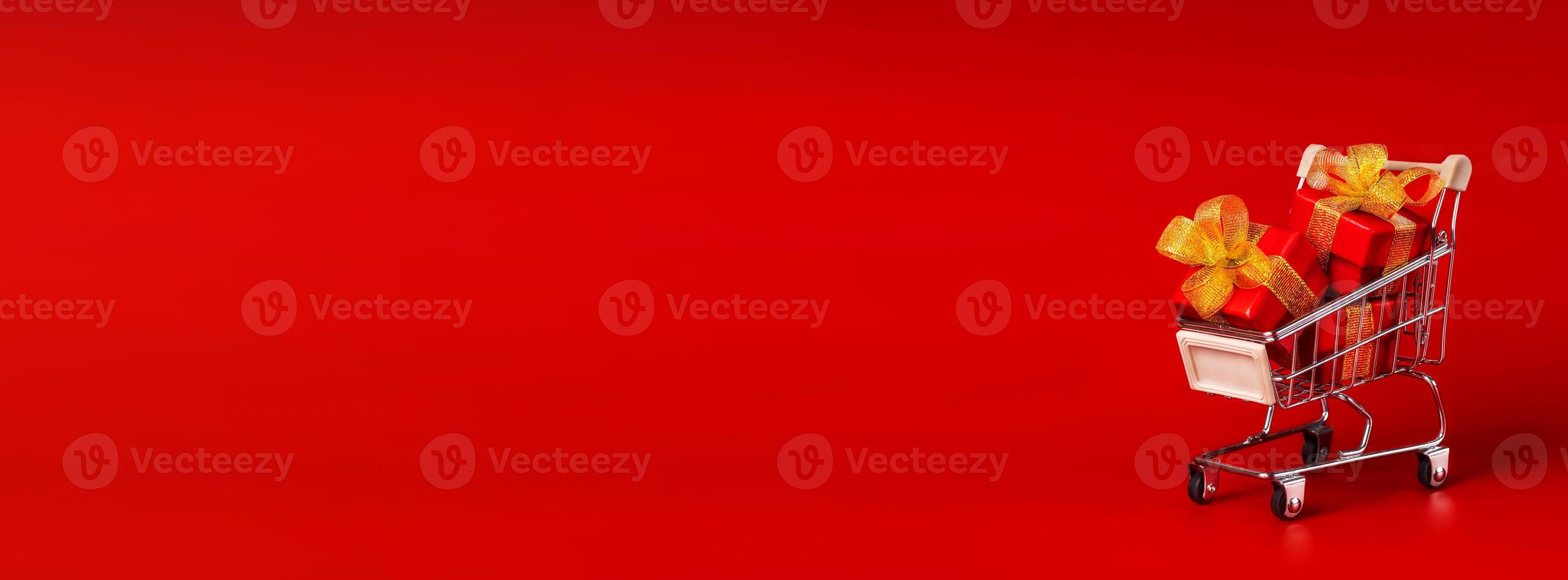 Supermarket trolley with red box with gold bows. The concept of buying gifts for holidays and sales. Discounts, Black Friday. Red background, Copy space long horizontal banner photo