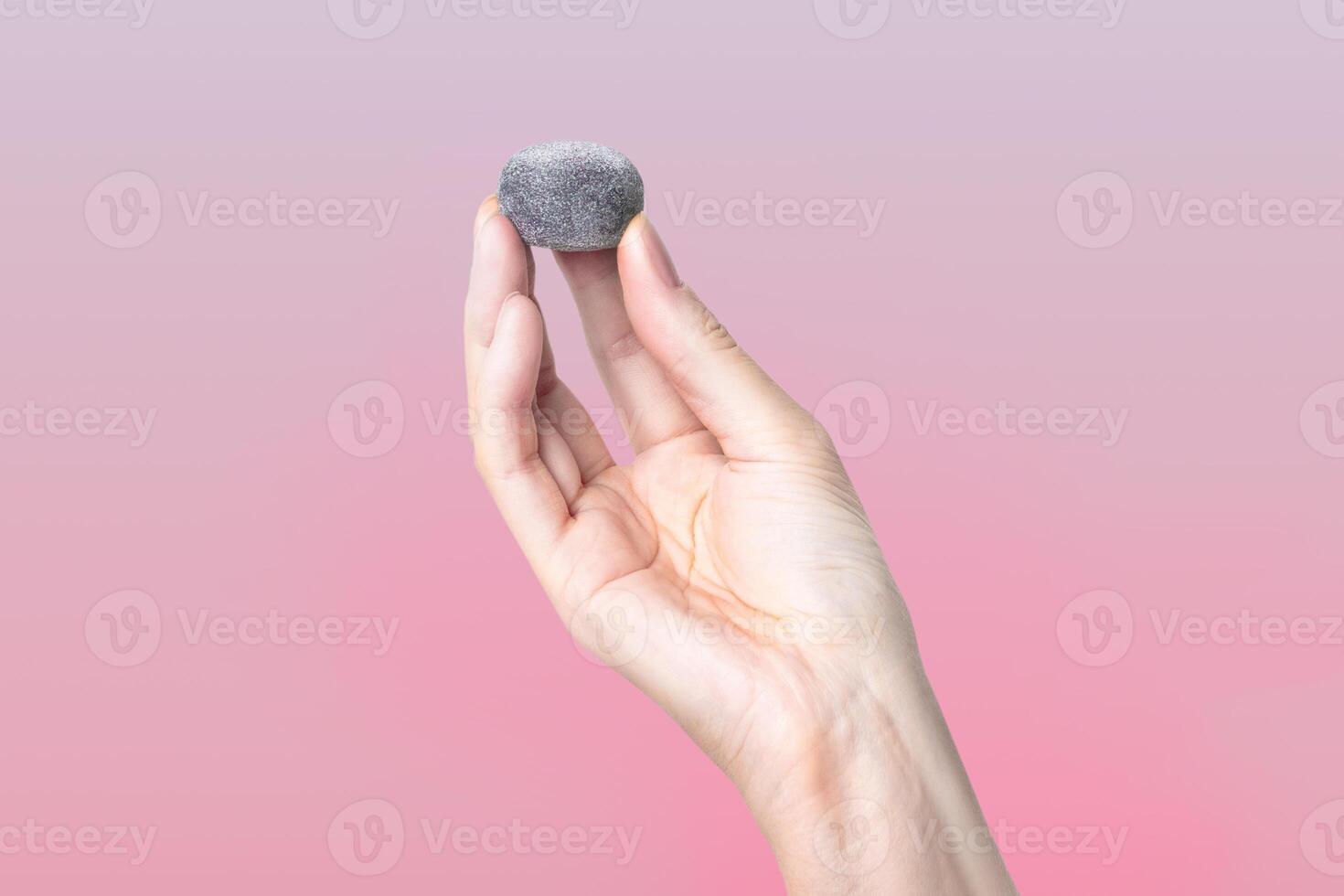 A woman's hand holds a black mochi candy, Isolated on pink gradient background photo
