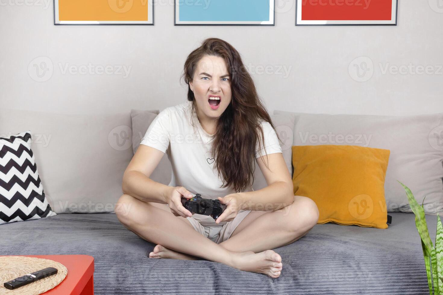 Brunette woman is holding a black joystick. Woman emotionally play game on the console. Woman upset. in home interior photo