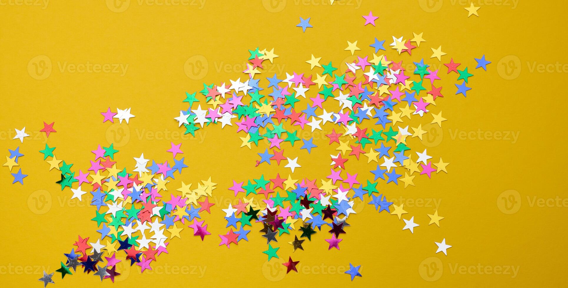 Scattered multicolored glitter confetti in star shape on yellow background photo