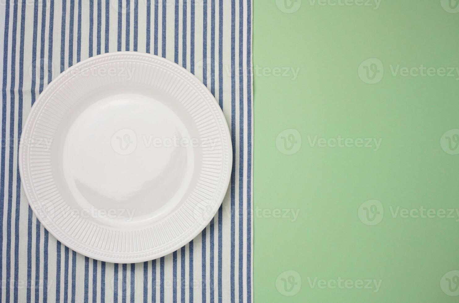 Empty round ceramic plate and blue kitchen towel on green background, top view photo