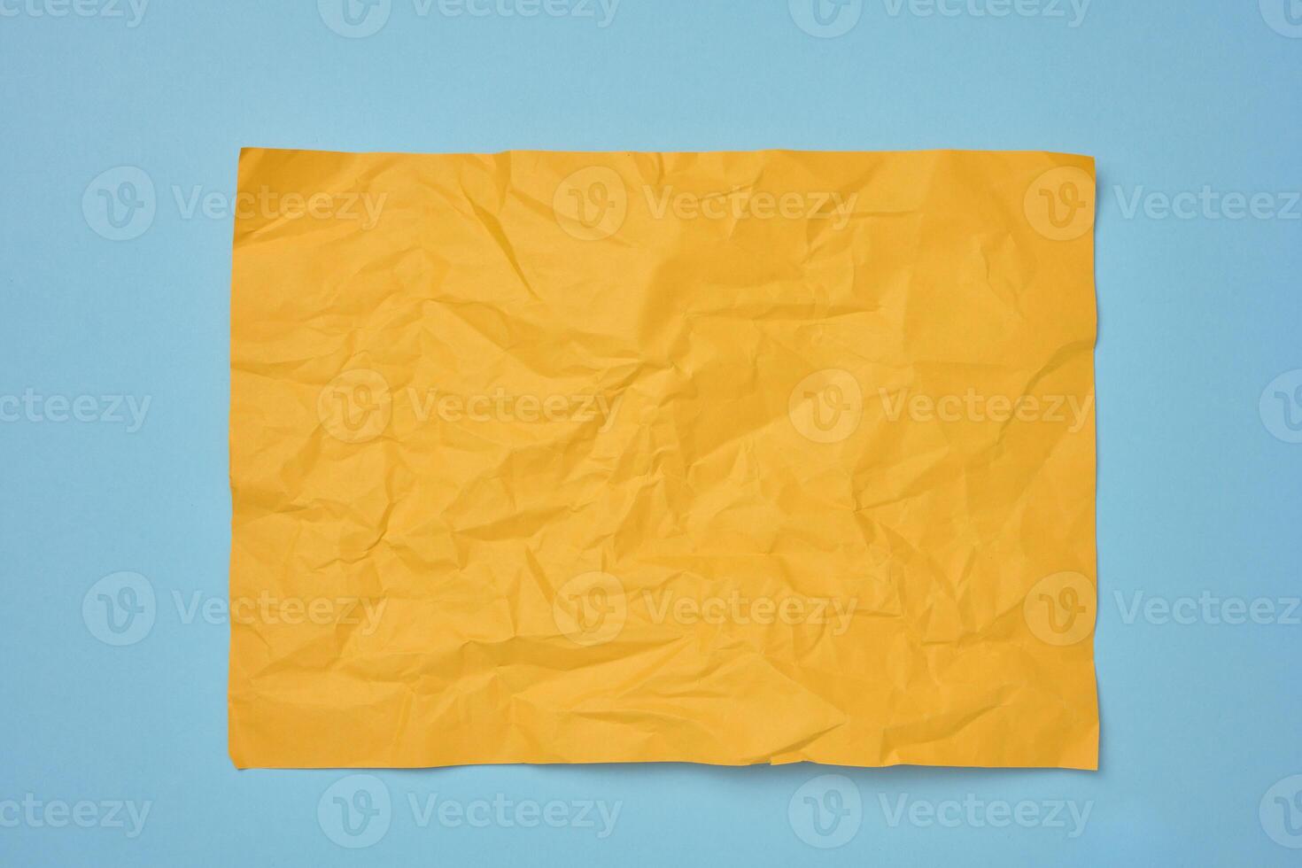 Crumpled rectangular sheet of yellow paper on a blue background, top view. Place for inscription photo