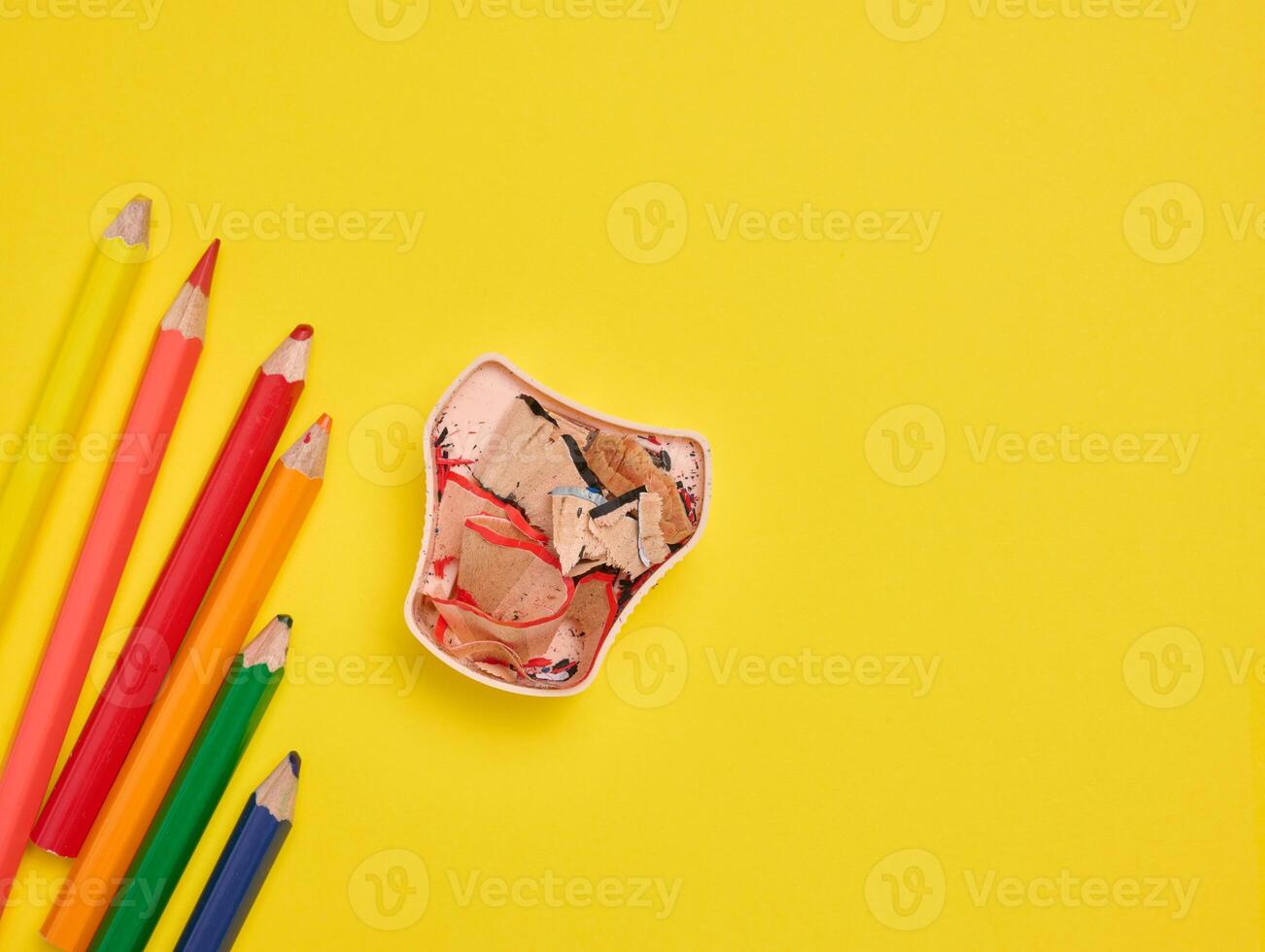 Multicolored wooden pencils and sharpener on yellow background, top view photo