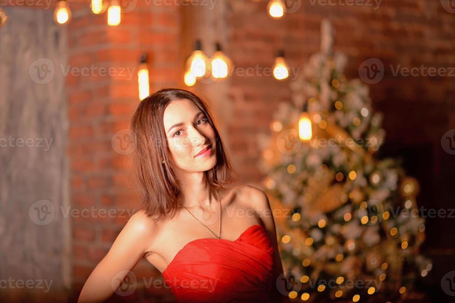 Christmas photo shoot. A girl wearing a red dress poses at the blurred background of a decorated New Year tree. Christmas and New Year celebration concept
