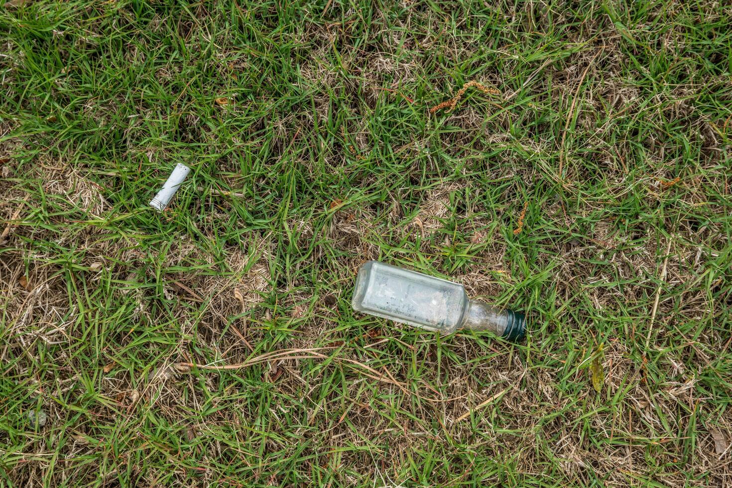 Liquor bottle and cigarette laying on the ground photo