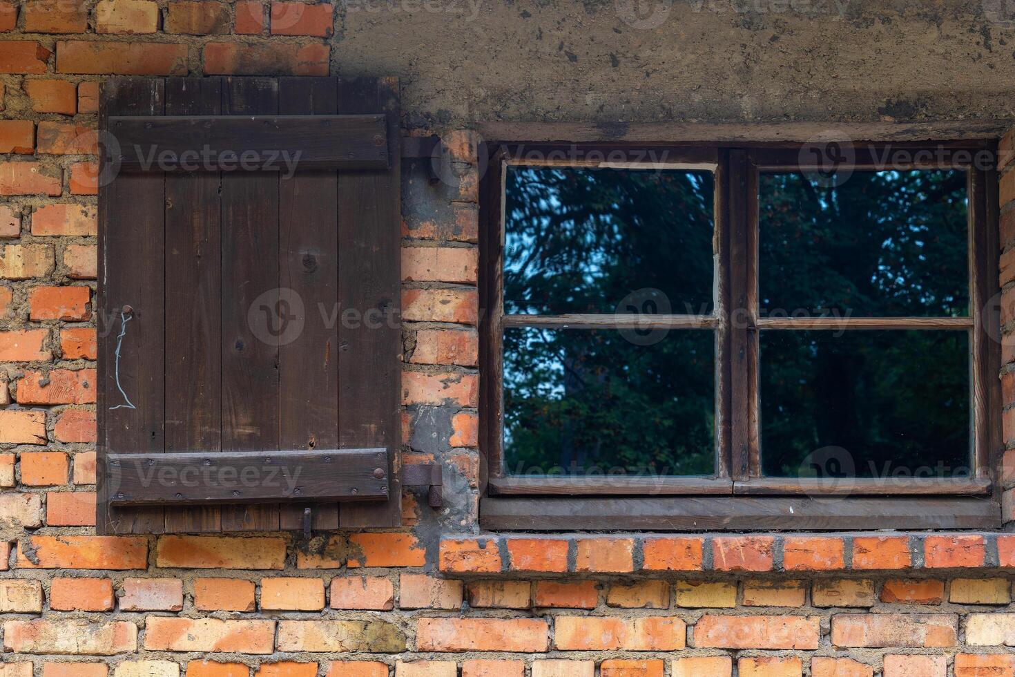 window with a wooden shutter sits in front of a brick wall photo