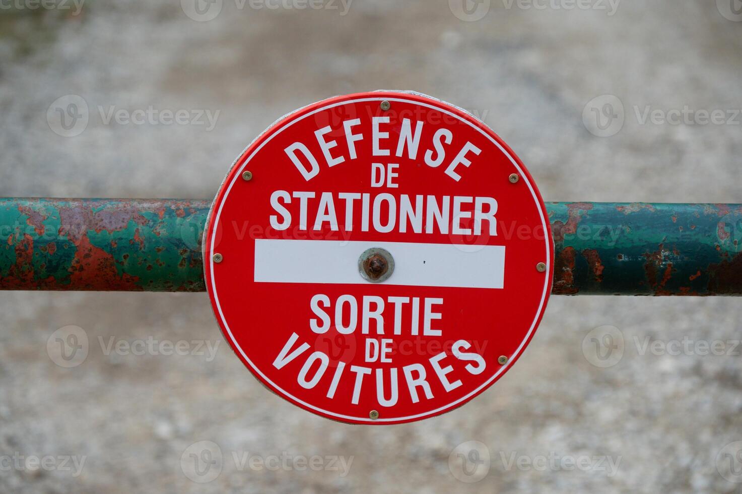 In the image, there is a weathered gate with a red sign in French indicating no parking photo