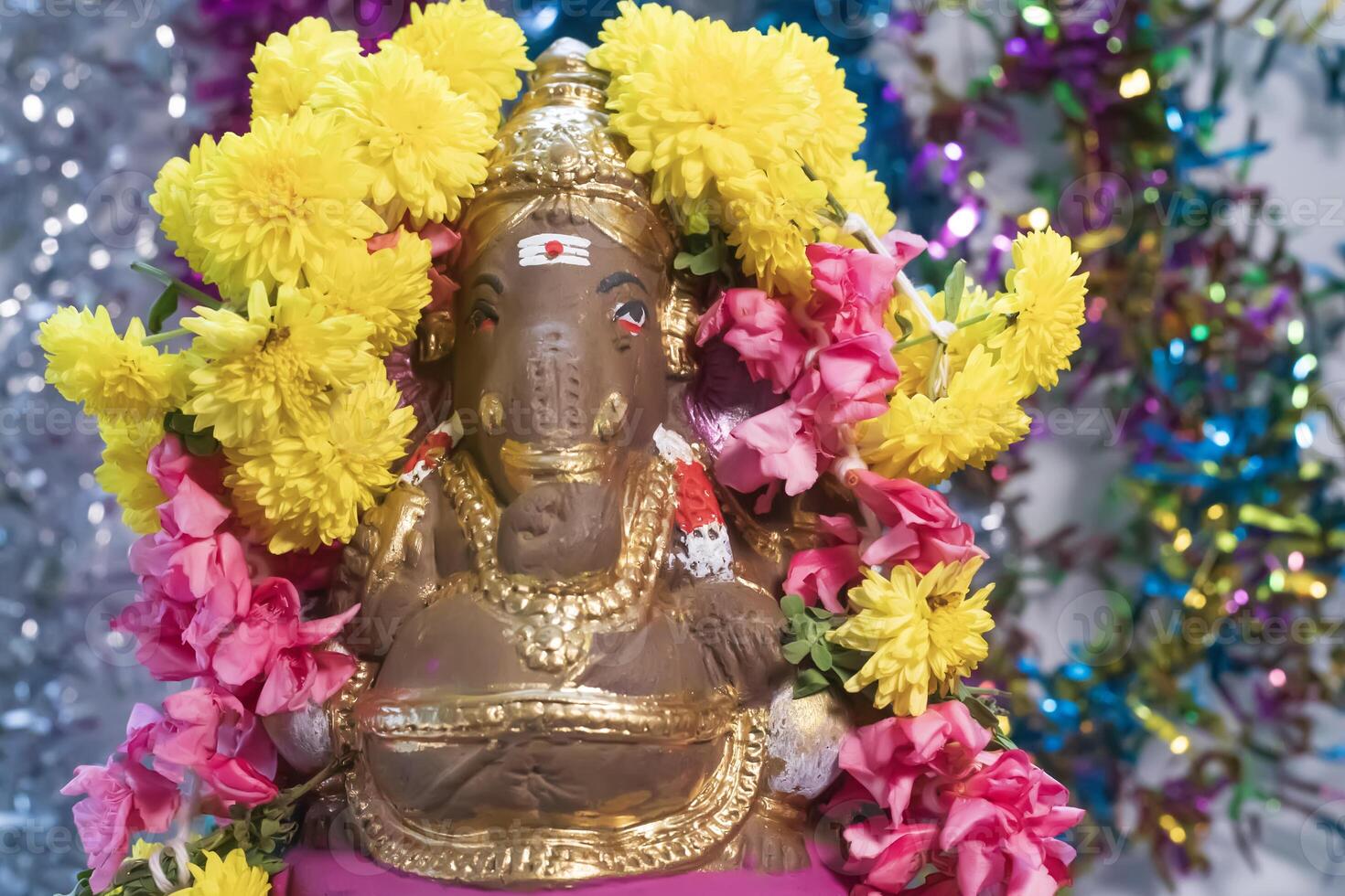 Hindu god Ganesha statue made of clay decorated with flower garlands on bokeh effect background. Closeup photo