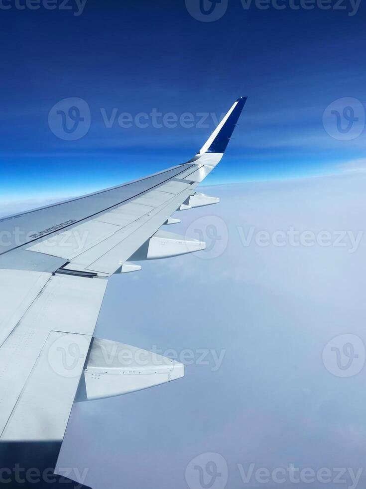 Airplane wing flying above the clouds on sunny day photo