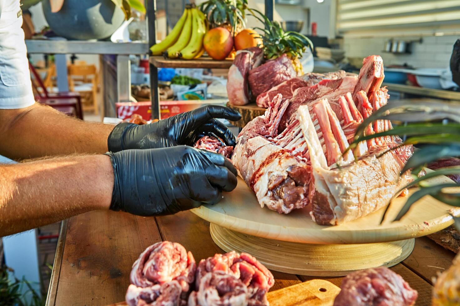 A chef wearing black gloves arranges a rack of raw lamb on a wooden board surrounded by various cuts of meat, preparing for cooking. photo