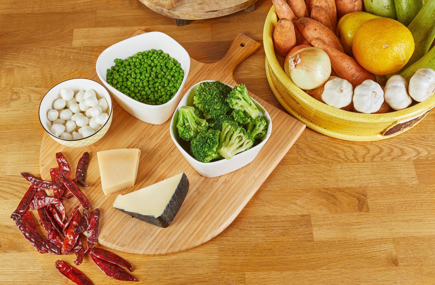 A wooden cutting board arranged with an assortment of fresh vegetables, cheeses, and peppers, ready for cooking or meal preparation photo