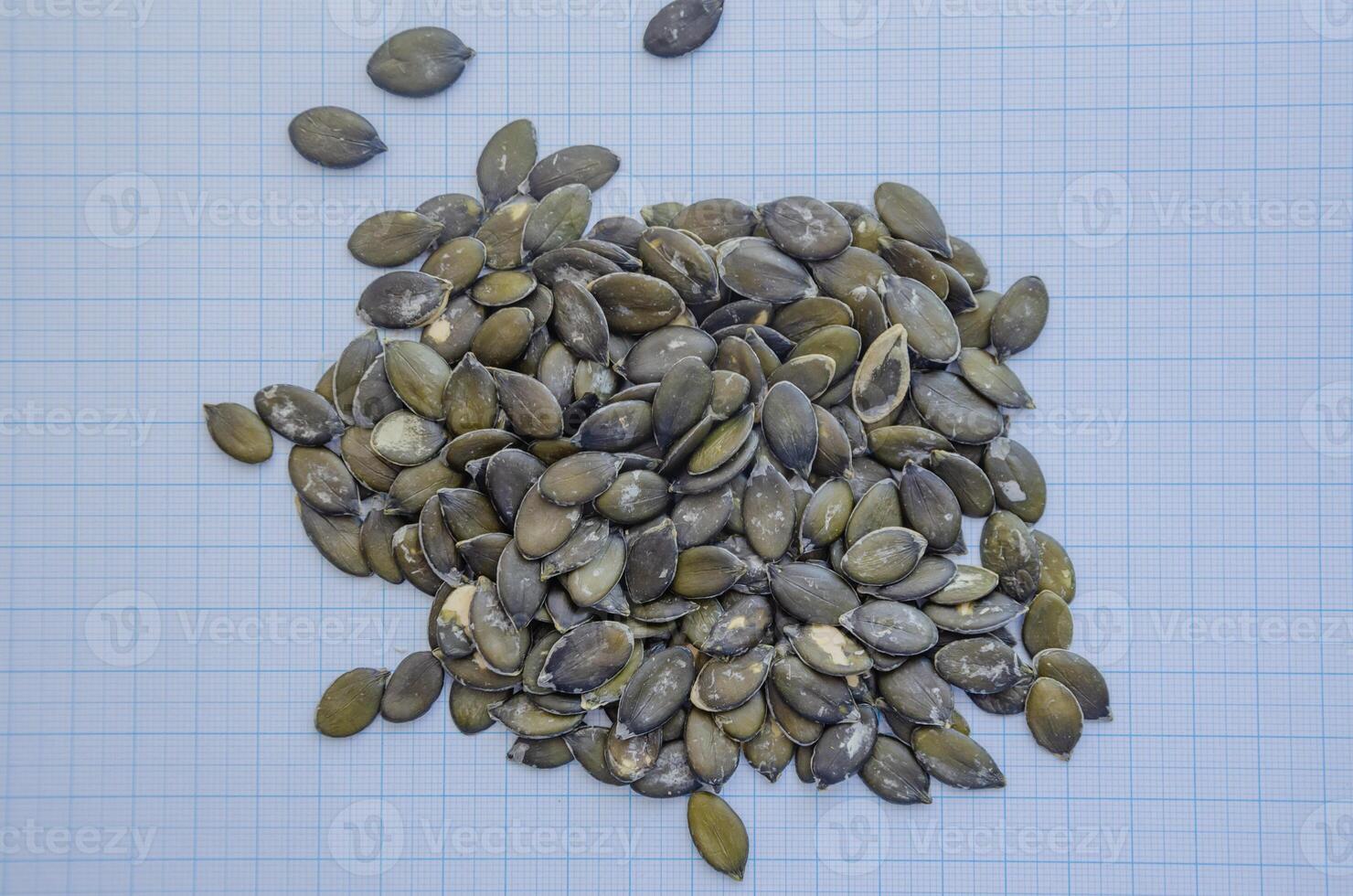 A pile of pumpkin seeds on a millimeter background for a seed-size view. Gymnosperm pumpkin seeds. High quality photo