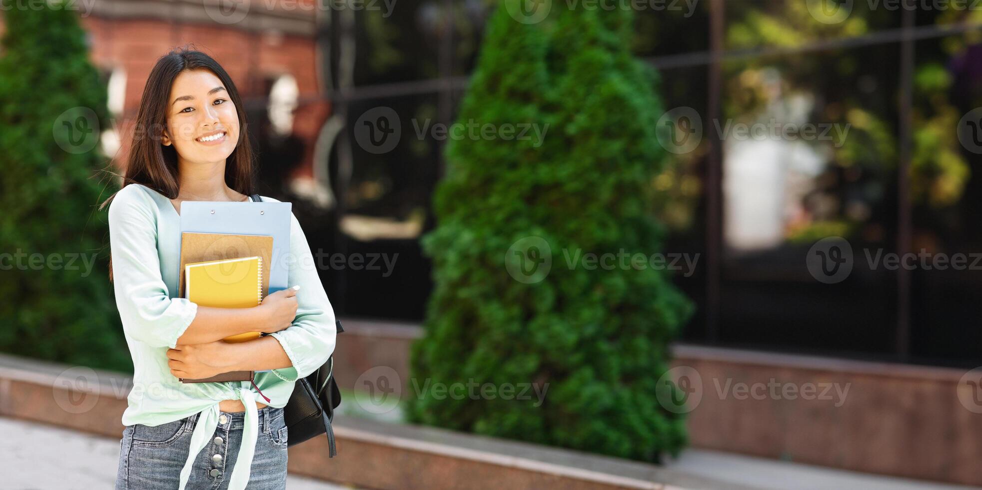 Education Concept. Attractive asian student girl with backpack and notebooks standing and smiling over university background, free space photo